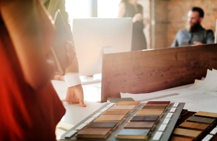 Hands choosing between wood samples and finishes laid out on a work table