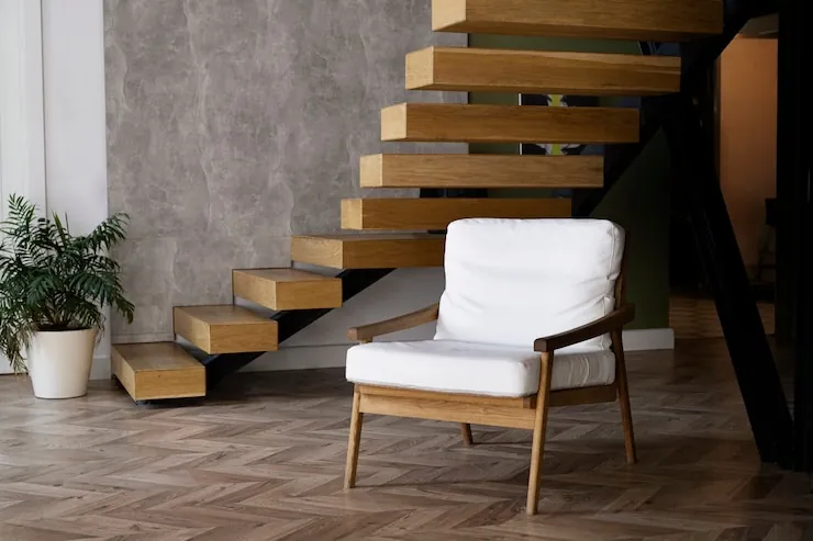 Staircase with solid wood treads fixed to the wall, next to a white armchair and a plant