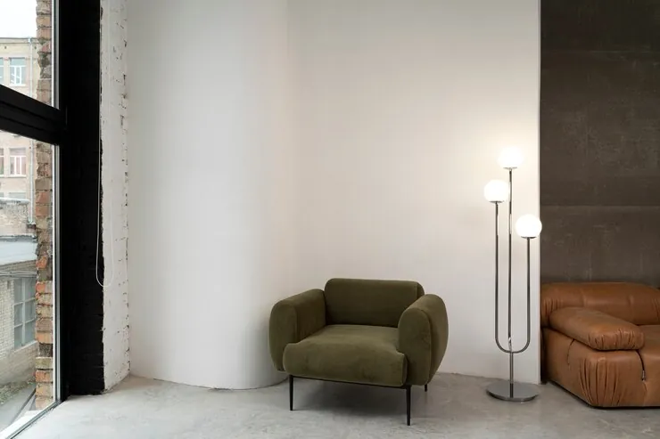 Minimalist room with white walls, a green armchair, a floor lamp and a leather bench